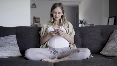 Calm-pregnant-woman-listening-to-music-from-smartphone